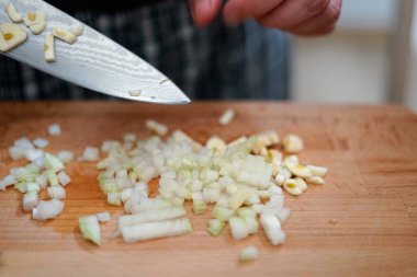 Ahşap kesme tahtasındaki taze malzemeleri ustalıkla doğrayan bir aşçı elinin yakın çekimi, aşçılık hazırlıklarını vurguluyor..