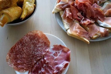 Ahşap bir masa üzerinde dilimlenmiş et ve kruvasan güzel bir düzenleme, bir gurme kahvaltısı veya şarküteri tahtası için mükemmel..