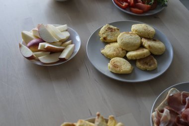 Dilimlenmiş elmalar, kabarık bisküviler, taze domatesler ve ahşap bir masa üzerindeki diğer aksesuarların yer aldığı enfes bir kahvaltı düzenlemesi..