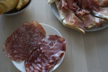 Tahta bir masa üzerinde salam ve prosciutto da dahil olmak üzere çeşitli pişmiş etler sergileniyor. Şarküteri tahtaları için mükemmel..