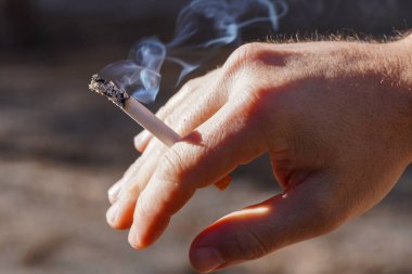 Elin ormanın arka planında yanan bir sigara tutuyor. Yakın plan.