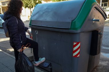 Sokakta çöp kutusuna torba atan genç bir kadın..