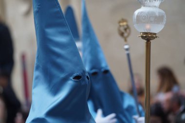 Nasıralı bir deniz feneriyle İspanya 'da kutsal bir hafta yürüyüşünde yürürken, diğer bir tanesi arka planda mavi renkte yürüyor..