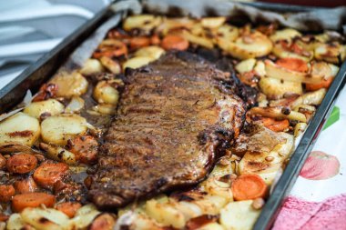 Patates, sarımsak, havuç ve soğanla çevrili yemek tepsisi fırından yeni çıkarılmış, tadımlık hazır.