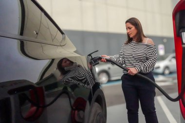 Bir kadın, 20 Nisan 2025 'te Nueva Apartman Merkezi' ndeki Tesla şarj istasyonunun pillerini doldurmak için siyah elektrikli arabasının şarjını yerleştiriyor..