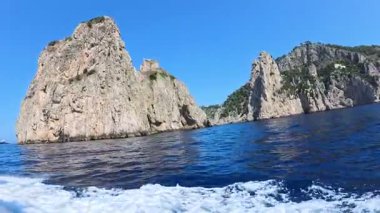 Capri 'nin Faraglionisi, kristal berrak sudan çıkan iki büyük taş, güneşli bir yaz gününde mavi gökyüzü ile tekne gezintisine çıkıyor.