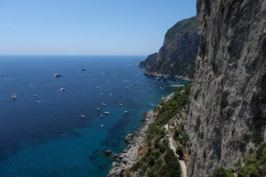 Yolların aktığı Capri Adası 'nın kayalıkları, açık ve güneşli bir yaz gökyüzü olan turist tekneleriyle dolu mavi bir deniz.