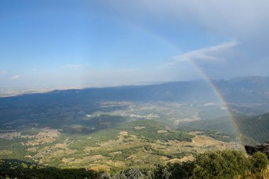 Rainbow seen from the top of the mountain, overlooking a large valley on a stormy autumn day