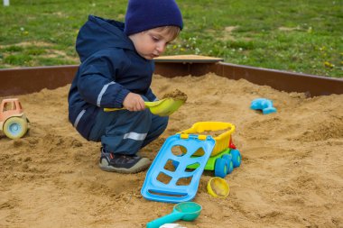 Kum havuzunda yeşil oyuncak malası ve mavi arabasıyla oynayan küçük bir çocuk. Yüksek kalite fotoğraf
