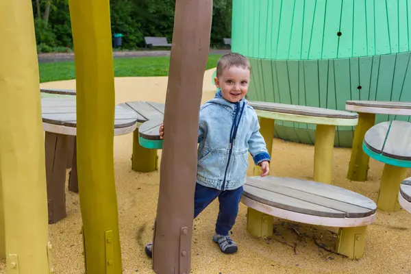 Kot elbiseli çıplak ayaklı küçük bir çocuk modern bir ahşap oyun alanında yürüyor. Yüksek kalite fotoğraf