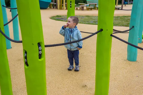 Kot elbiseli çıplak ayaklı küçük bir çocuk modern bir ahşap oyun alanında yürüyor. Yüksek kalite fotoğraf