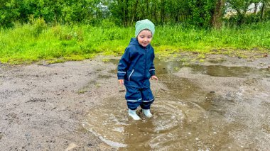 Çocuk lastik botlar ve su geçirmez bir giysiyle su birikintilerinde koşuyor. Yüksek kalite fotoğraf