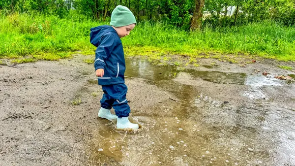 Çocuk lastik botlar ve su geçirmez bir giysiyle su birikintilerinde koşuyor. Yüksek kalite fotoğraf