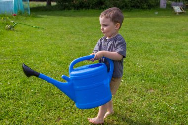 Çocuk bir seranın yakınındaki bir meyve sulama kutusundan sebze bahçesini suluyor. Yüksek kalite fotoğraf