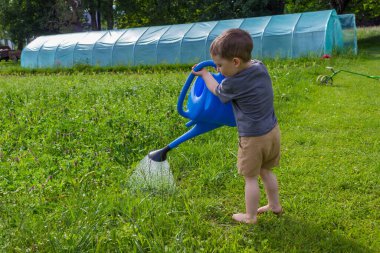 Çocuk bir seranın yakınındaki bir meyve sulama kutusundan sebze bahçesini suluyor. Yüksek kalite fotoğraf