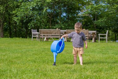 Çocuk bir seranın yakınındaki bir meyve sulama kutusundan sebze bahçesini suluyor. Yüksek kalite fotoğraf