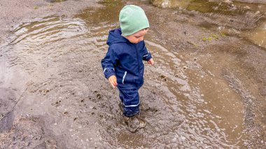Su geçirmez giysi ve lastik botlarla su birikintilerinde koşan küçük bir çocuk. Yüksek kalite fotoğraf