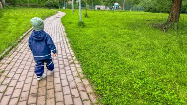 Çocuk yağmurda yolda su geçirmez bir takım elbise ve lastik botlarla yürüyor. Yüksek kalite fotoğraf