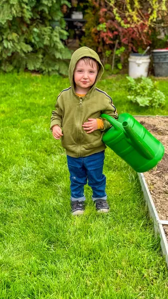 Çocuk bir seranın yakınındaki bir meyve sulama kutusundan sebze bahçesini suluyor. Yüksek kalite fotoğraf