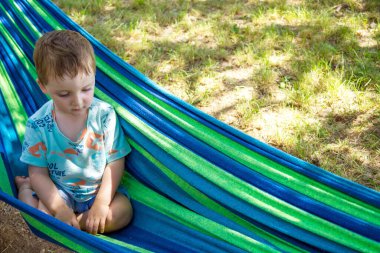 Sevimli küçük çocuk ağaçların gölgesinde mavi-yeşil hamakta dinleniyor. Yüksek kalite fotoğraf