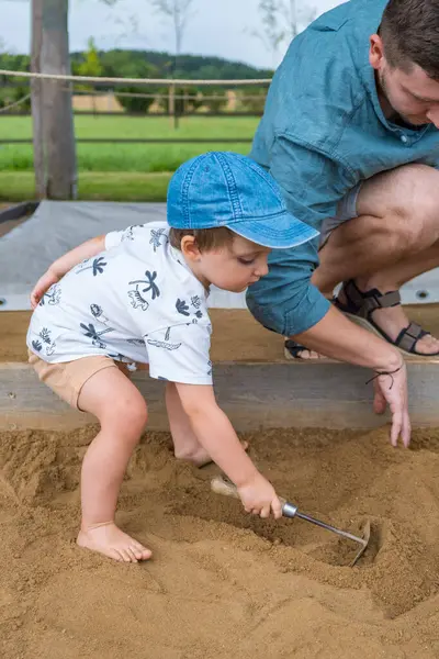 Baba ve oğlu arkeoloji parkındaki kum havuzunda tırmıkla kazı yapıyorlar. Yüksek kalite fotoğraf
