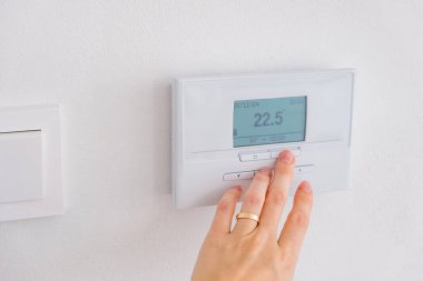 Duvardaki dijital termostatı oda sıcaklığını kontrol etmek için ayarlıyorum. Yüksek kalite fotoğraf