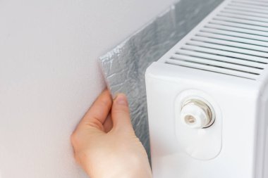 Isıyı odaya yansıtmak için radyatörün arkasına el termal yalıtımı yerleştiriliyor. Yüksek kalite fotoğraf