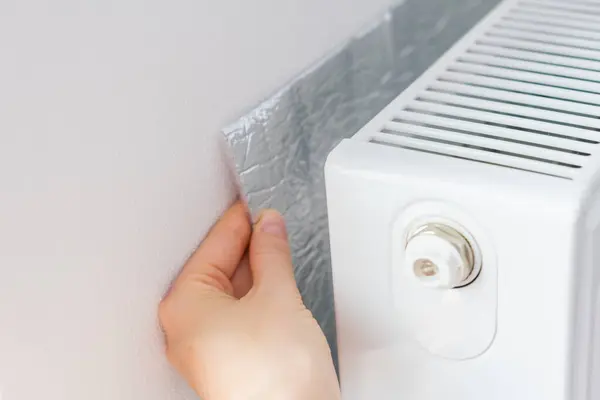 Isıyı odaya yansıtmak için radyatörün arkasına el termal yalıtımı yerleştiriliyor. Yüksek kalite fotoğraf