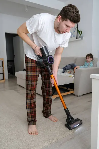 Genç adam kablosuz elektrik süpürgesi kullanıyor, verimli ve modern ev temizliği yapıyor. Yüksek kalite fotoğraf