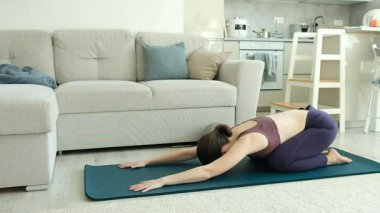 Evde yoga minderinin üzerinde uzanan bir kadın, rahatlıyor ve esnekliğini geliştiriyor. Yüksek kalite 4k görüntü