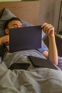 Rahatlamış bir adam dizüstü bilgisayarla yatakta takılıyor. cep telefonu ve wHigh kalitesinde fotoğraf