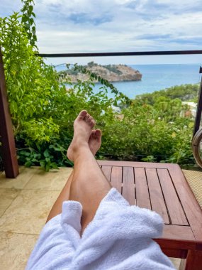  Kadın bacakları, sahil kenarındaki otel ya da apartmanın balkonunda sandalyede dinleniyor. Yüksek kalite fotoğraf