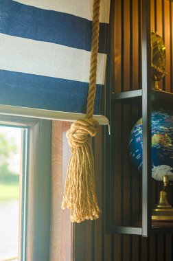 Elegant curtain with nautical rope tie-back beside a globe in marine style room. High quality photo clipart