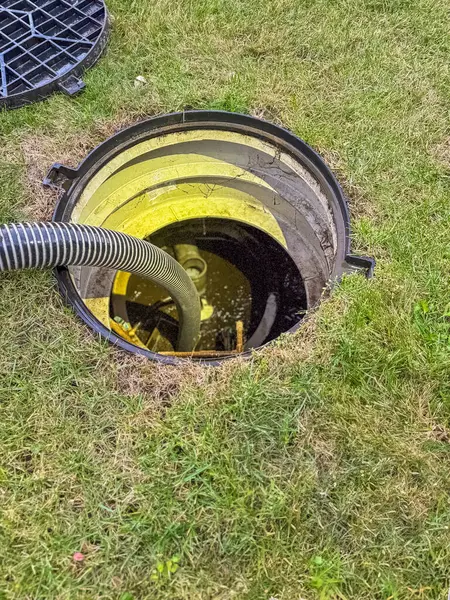 Kanalizasyon kapağını açtı ve lağım çukurunu temizlemek için bir hortum yerleştirdi. Yüksek kalite fotoğraf