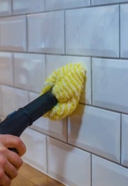 Man cleaning white tile wall with a yellow microfiber cloth and steam cleaner. High quality photo clipart