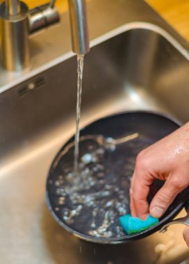  Mavi bir süngerle paslanmaz çelik bir lavaboda siyah bir tavayı yıkamak. Yüksek kalite fotoğraf