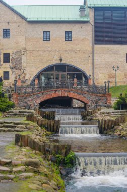  Taştan köprü çağlayan akarsuyun üzerinde kavis çiziyor ve tarihi tuğla bir binaya çıkıyor. Yüksek kalite fotoğraf