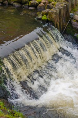 Küçük şelalenin ahşap direklerin üzerine düşmesi sakin bir manzara yaratıyor. Yüksek kalite fotoğraf