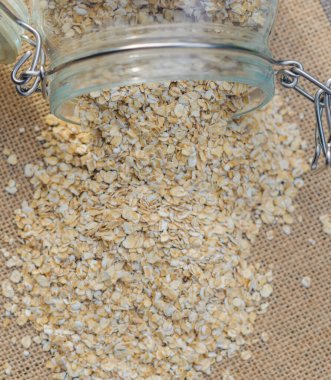 Rolled oats spilling from glass jar onto a burlap surface, healthy food concept. High quality photo clipart