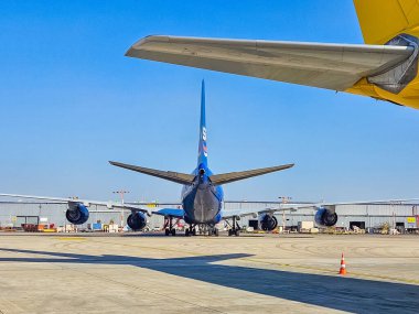 Blue passenger jet tail, seen from behind, parked on tarmac with yellow wing above. High quality photo clipart