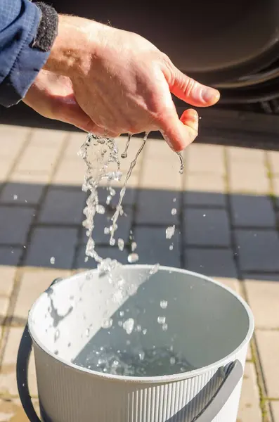 Adam Sunny Day 'de ellerinin arasından suyu sıkar ve kova içine temizler. Yüksek kalite fotoğraf