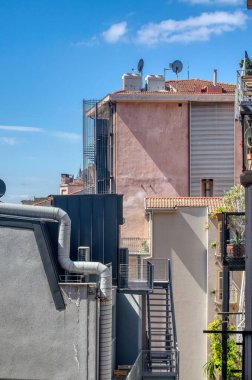 Mavi gökyüzünün altında uydu antenleri, havalandırmaları ve merdivenleri olan şehir çatıları. Yüksek kalite fotoğraf