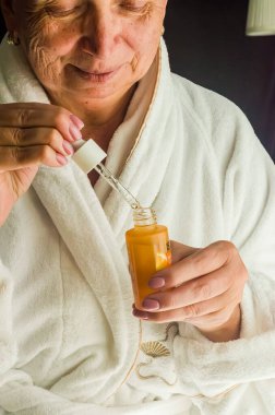 Bornozlu kadın, huzurlu bir ortamda yumuşak dokunuşla cilt serumu uyguluyor. Yüksek kalite fotoğraf