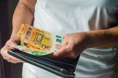 Kadın, iyi ışıklandırılmış bir ortamda cüzdanı tutarken avro banknotlarını sayıyor. Yüksek kalite fotoğraf