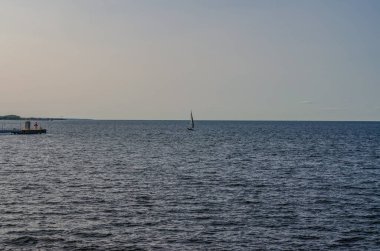 Yalnız yelkenli, Sakin Deniz 'de Yumuşak Günbatımı Gök Ufku' nun altında yüzüyor. Yüksek kalite fotoğraf