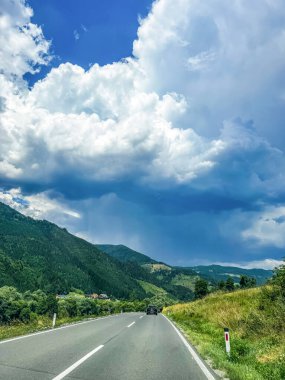 Güzel iki şeritli dağ yolu, yemyeşil tepeler ve dramatik beyaz bulutlarla uzaklara uzanıyor. Yüksek kalite fotoğraf