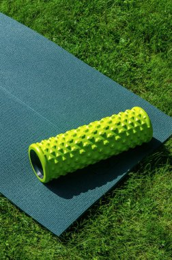 Çimenlerdeki yoga minderinde dinlenen yeşil köpük masaj silindiri fitness ve kas düzeltme egzersizleri için kullanılır. Yüksek kalite fotoğraf