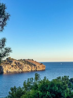 Ufukta bir yelkenli, seyahat, özgürlük ve doğayı temsil eden derin mavi okyanus suyuyla çevrili kayalık sahil uçurumunun manzarası. Yüksek kalite fotoğraf
