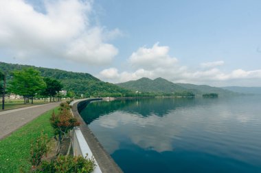 Park ve Toya Gölü ya da Toyako, Hokkaido, Japonya 'da egzersiz yapan insanlar mavi tonda ve su yüzeyinin, dağın ve gökyüzünün yansımasıyla