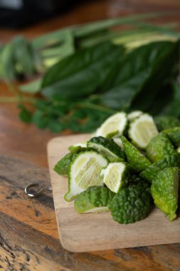 Dilimlenmiş kaffir kireç, ahşap tabak ve yeşil arka plan dikey çerçeve